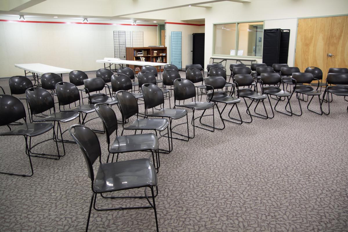 Carpeted meeting room with three rows of chairs and two white folding tables