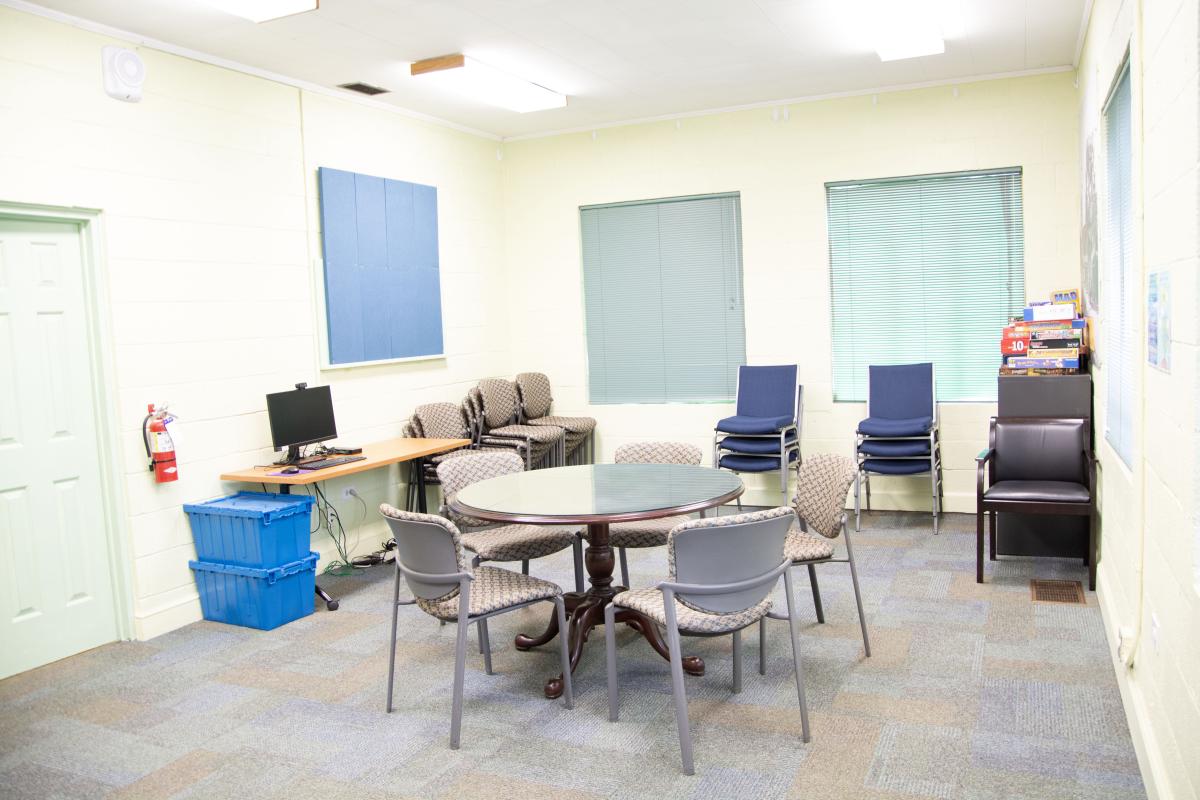 carpeted room with one round wooden table and multiple stacks of chairs